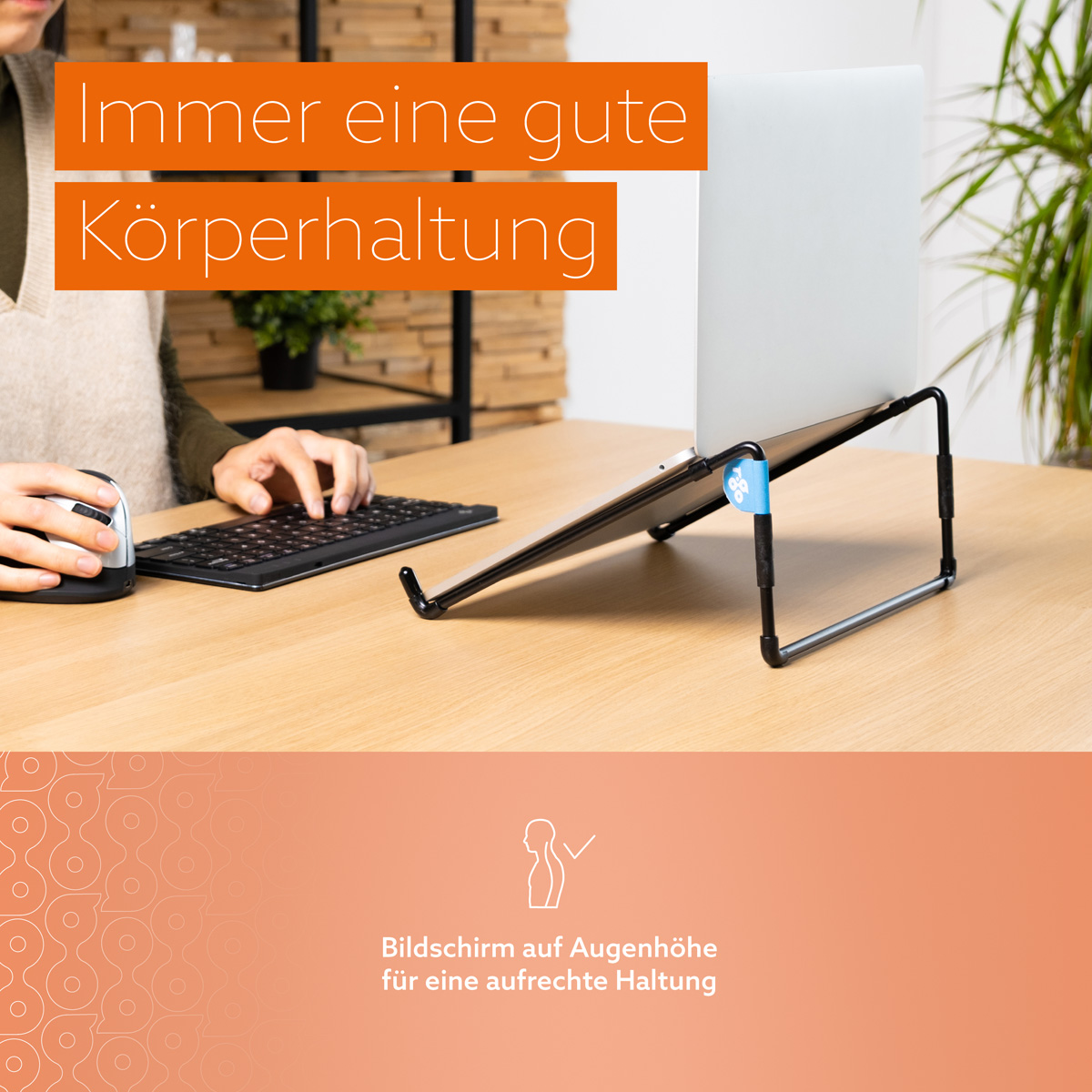 A laptop on a metal stand on a desk. Someone is typing on a keyboard and using a mouse nearby.