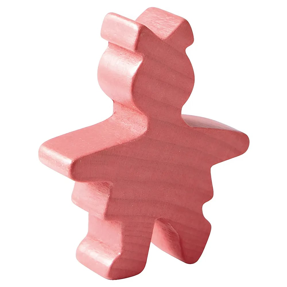 Eine kleine, pinke Holzschnitzfigur in Form eines Mädchens auf weißem Hintergrund.