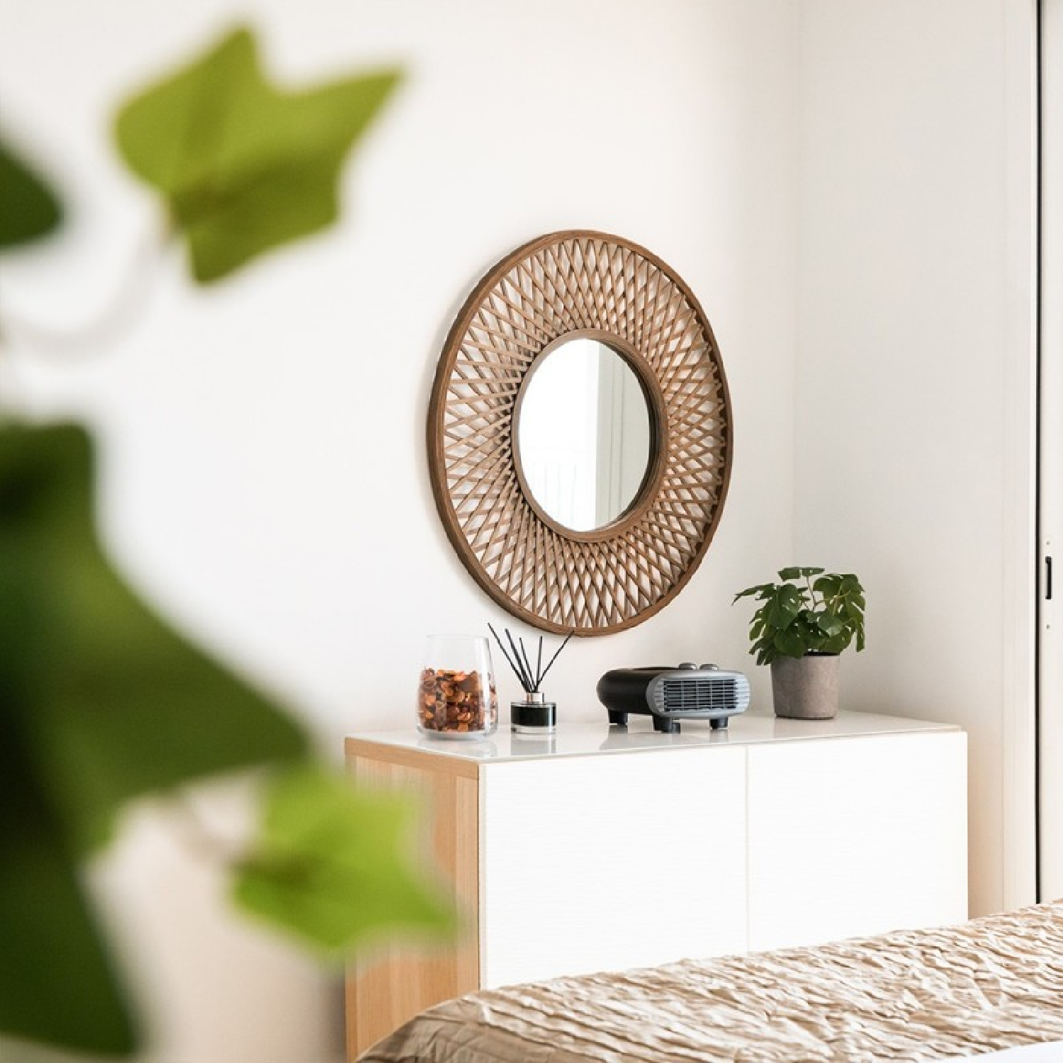 Un espejo de pared redondo de madera cuelga sobre una cómoda blanca con plantas y decoración.