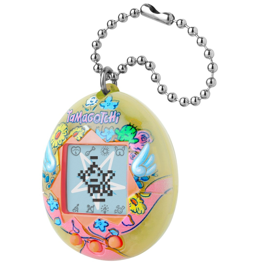 Żółty breloczek Tamagotchi w kwiaty ze srebrnym łańcuszkiem na białym tle.