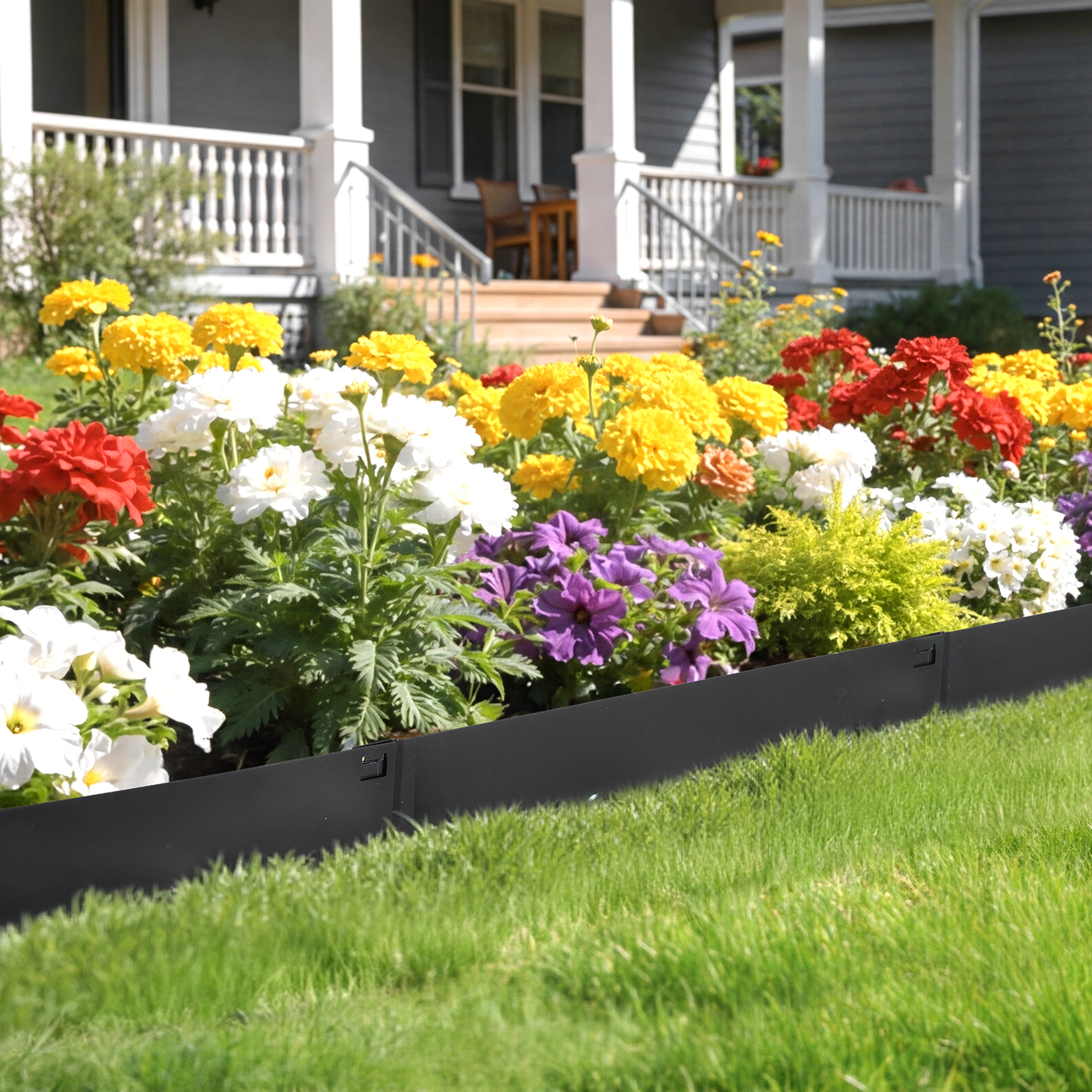 Eine schwarze Beetumrandung trennt den Rasen von einem bunten Blumenbett mit roten, gelben und lila Blüten.
