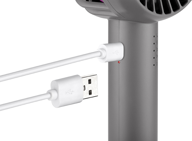 Ein grauer Handventilator wird mit einem weißen USB-Kabel aufgeladen, mit einer roten Kontrollleuchte.