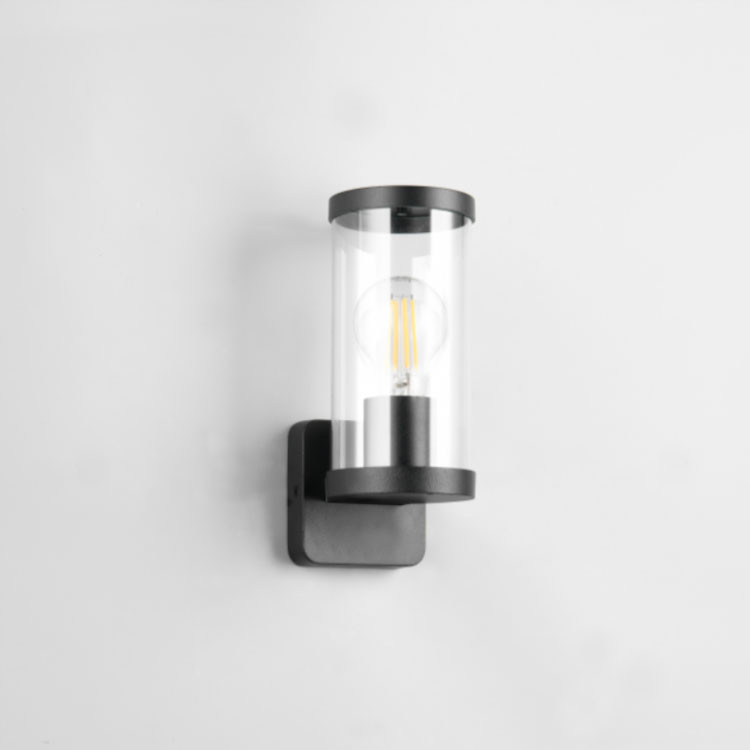 Lámpara de pared cilíndrica negra con vidrio transparente y bombilla visible en una pared blanca.