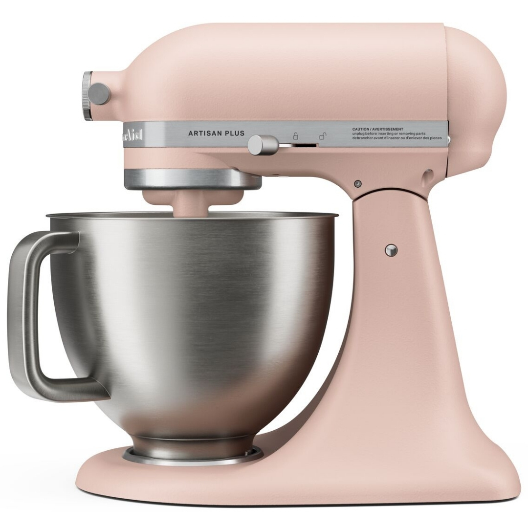 Beyaz arka planda paslanmaz çelik kasesi olan pembe bir KitchenAid Artisan Plus stand mikseri.