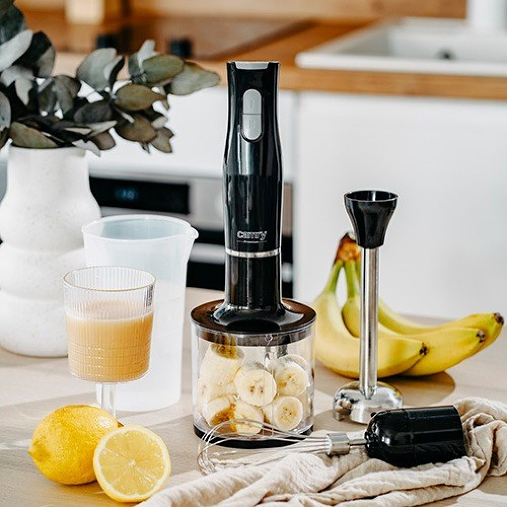 Czarny blender ręczny stoi na stole obok bananów, cytryn i szklanki smoothie w kuchni.