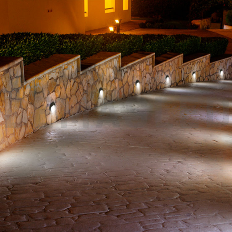 Muro de piedra iluminado a lo largo de un camino de noche con luz suave.