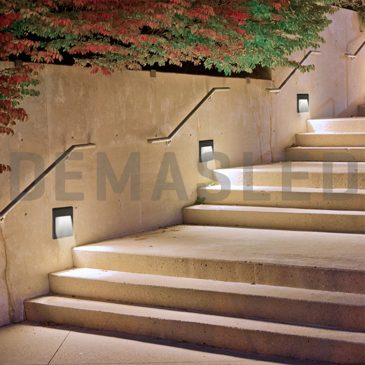 Escaleras de piedra al aire libre iluminadas por la noche con pasamanos y luces de pared.