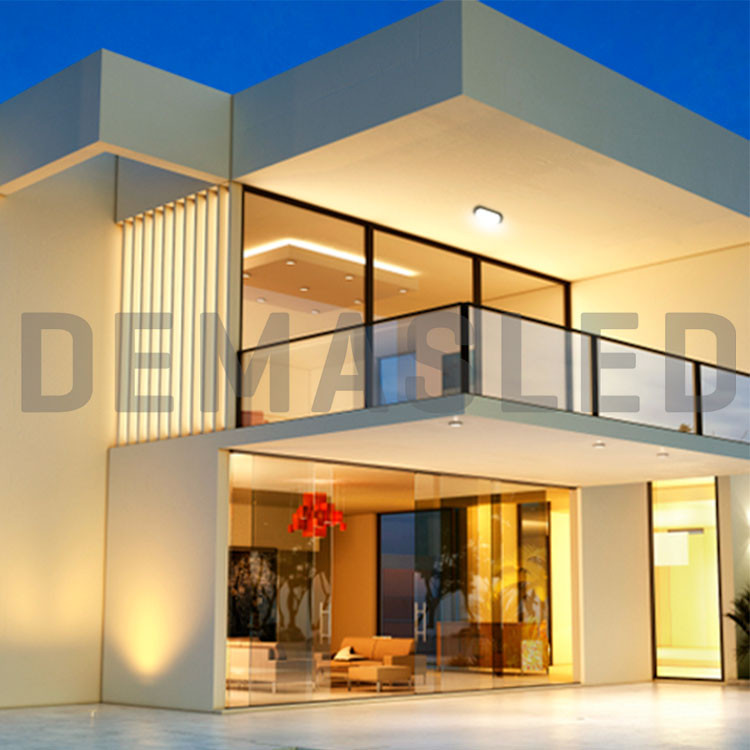 Villa moderna de dos pisos con gran fachada de vidrio, balcón y cálida iluminación exterior al atardecer.