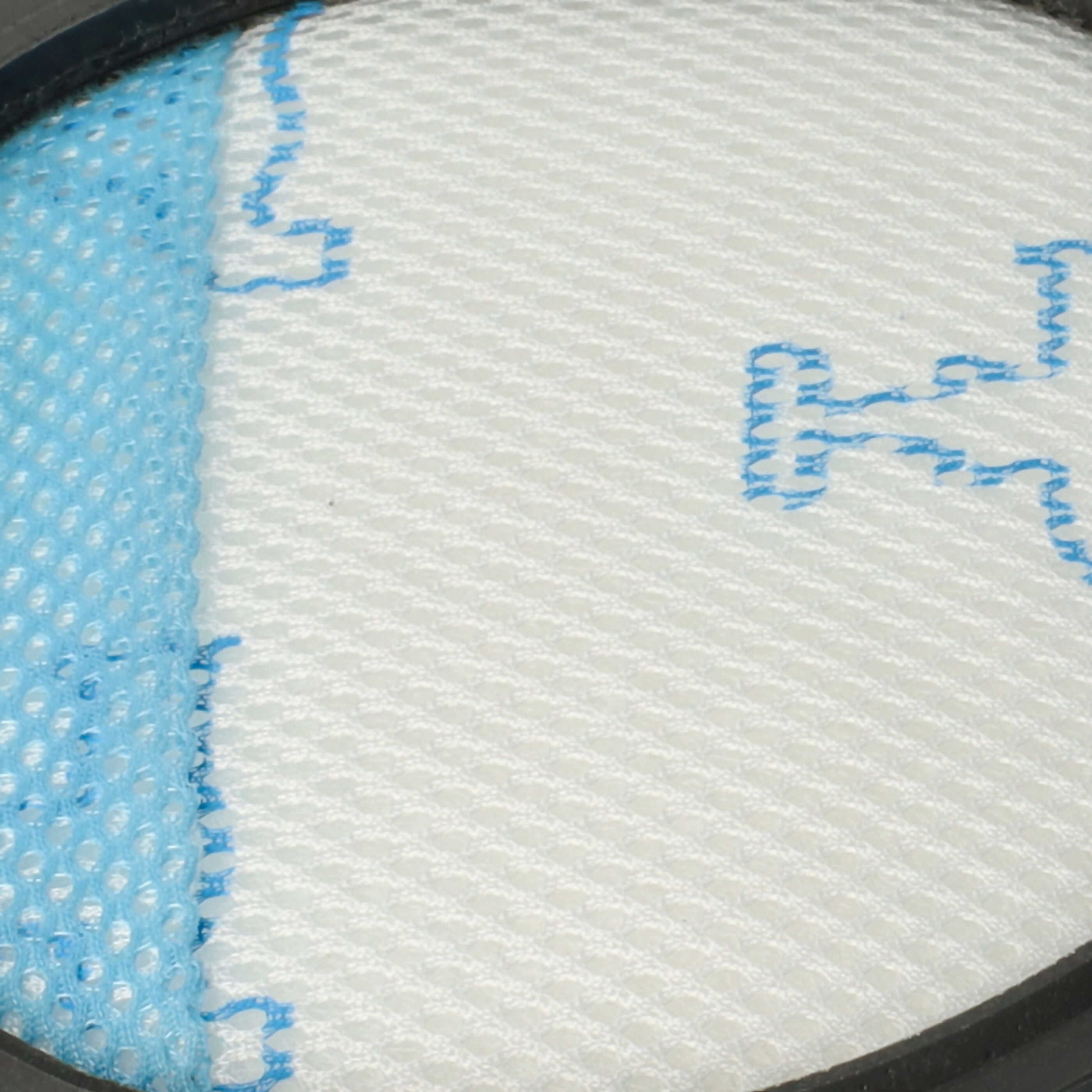 Runder weißer Filter mit feinem Netz und blauen Ziernähten in einem dunklen Gehäuse.