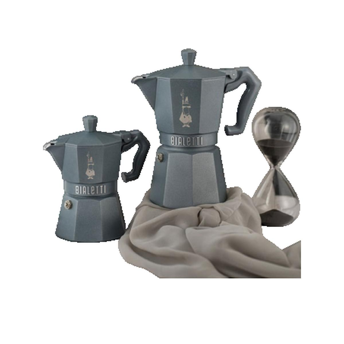 Due caffettiere moka Bialetti grigie e una clessidra su un panno.