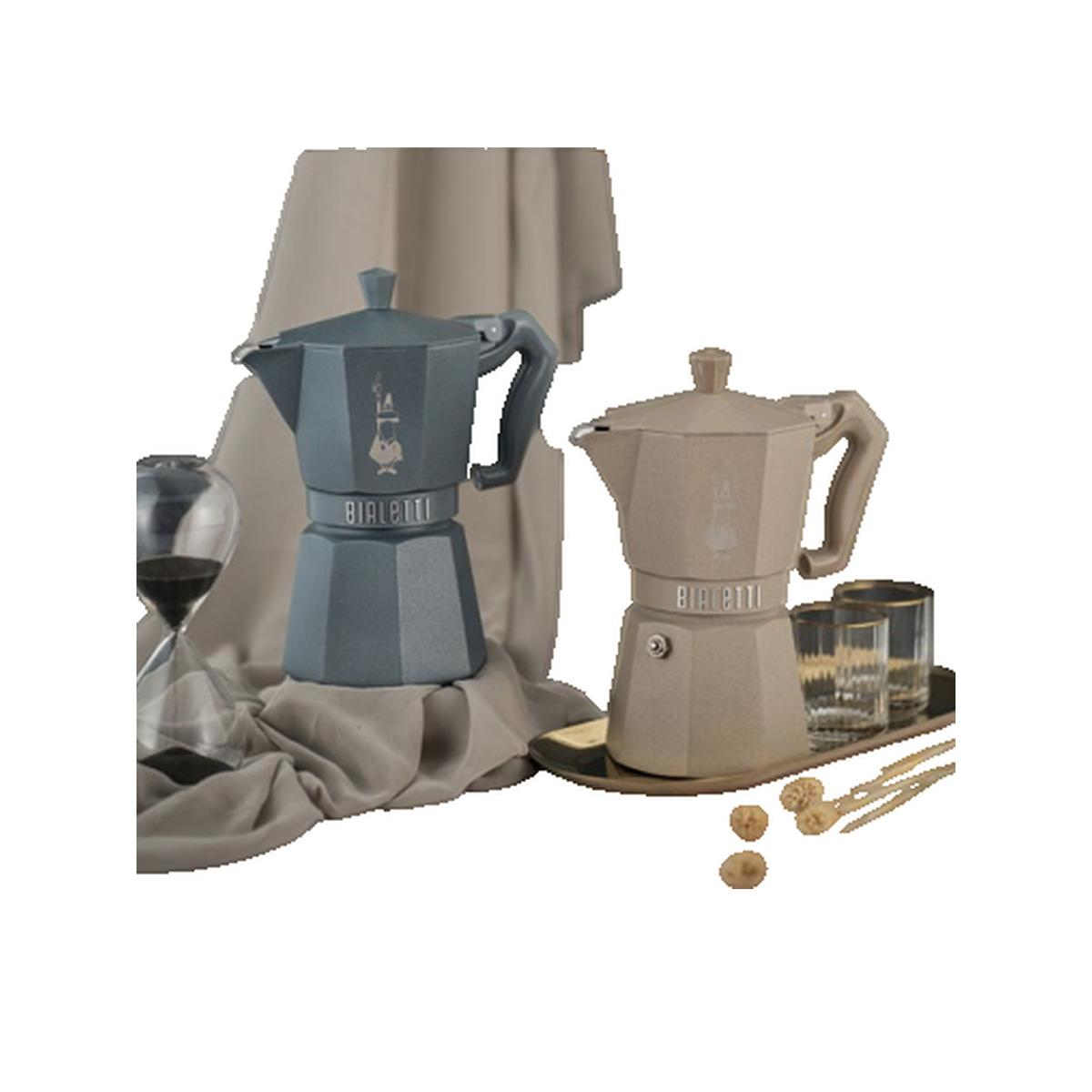 Caffettiere moka blu e beige con clessidra e bicchieri su sfondo grigio.