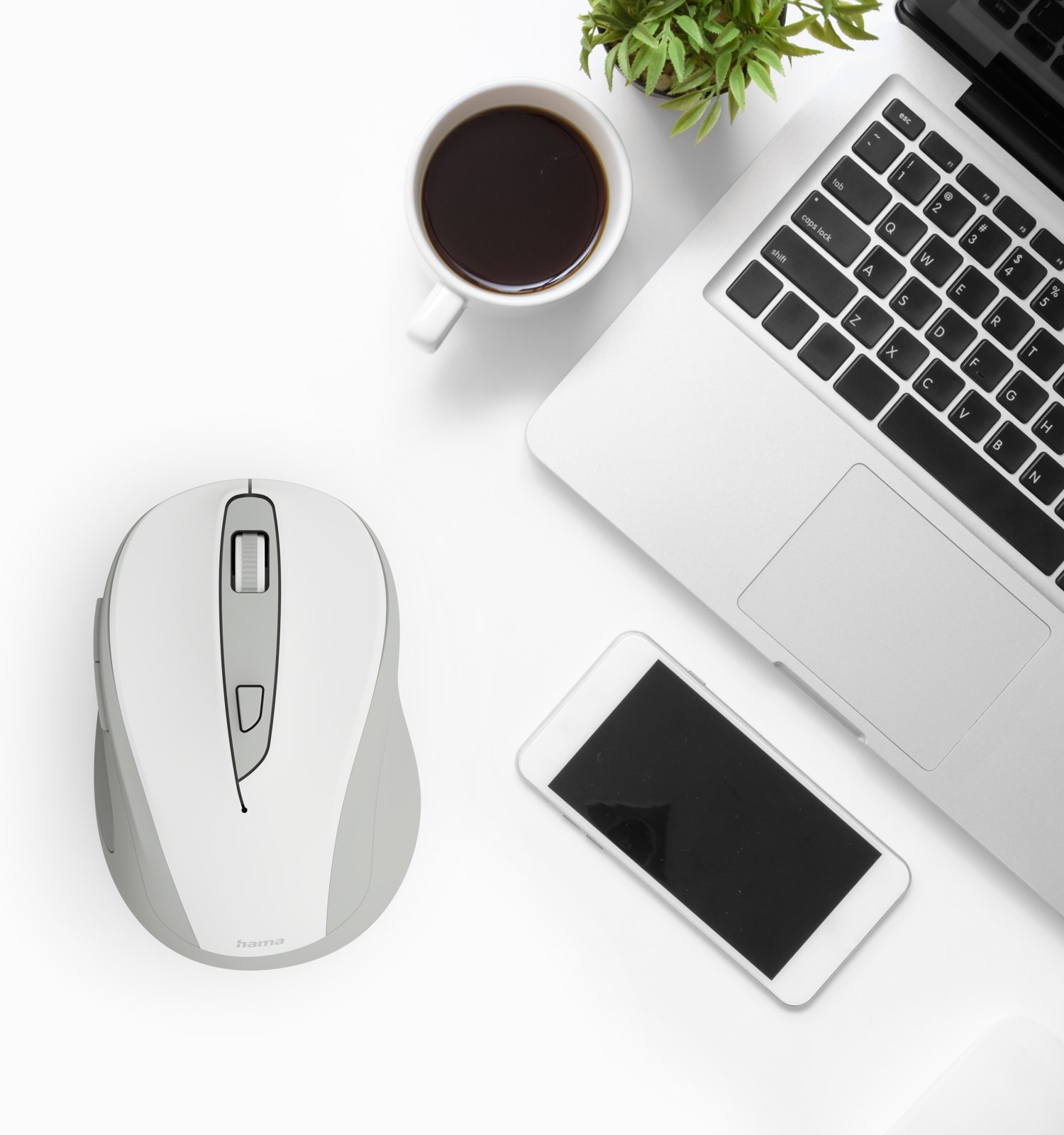 Draufsicht auf einen weißen Schreibtisch mit Laptop, weißer Maus, Smartphone, Kaffeetasse und einer kleinen Pflanze.