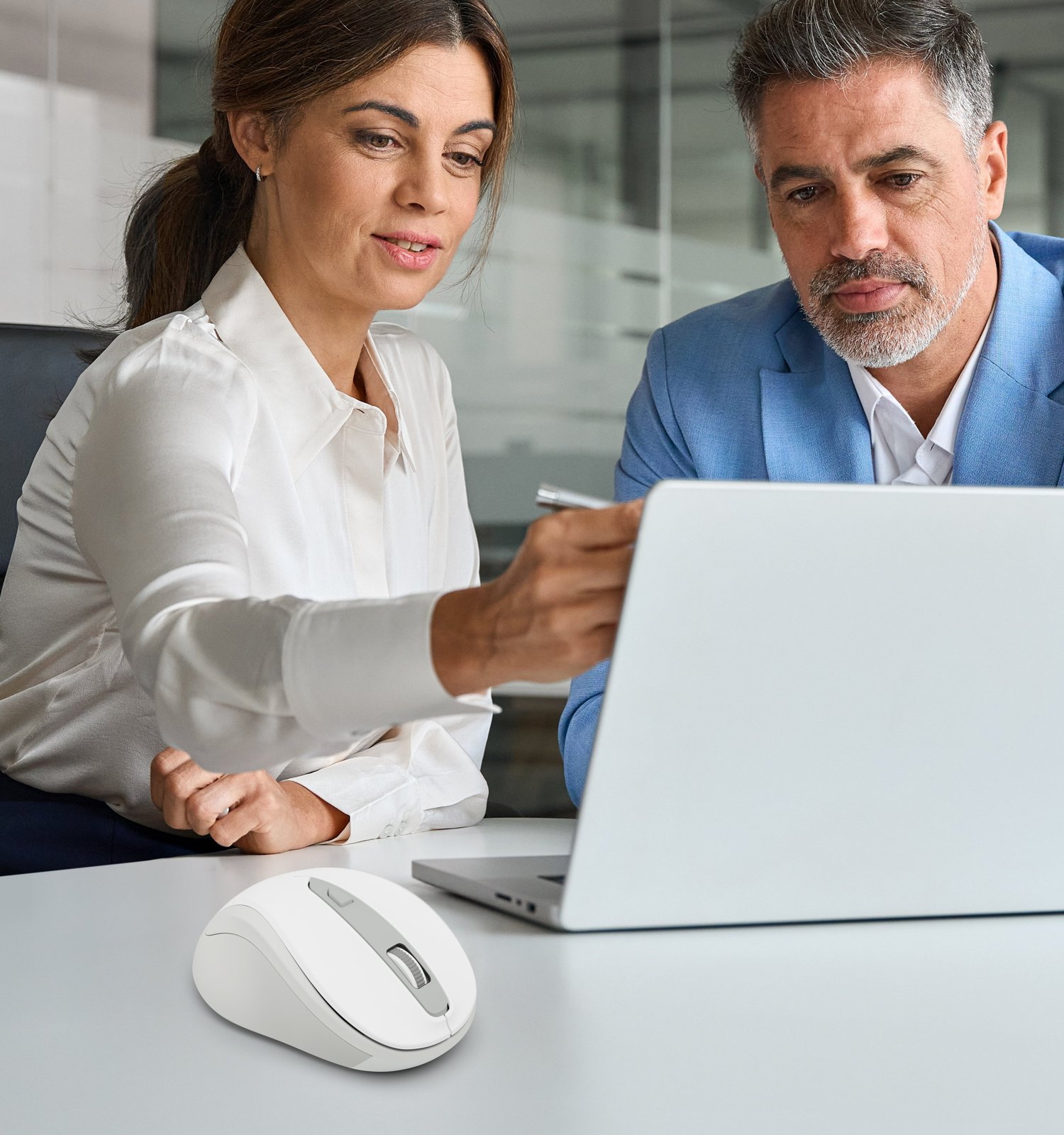 Eine Frau in Weiß und ein Mann in Blau sitzen im Büro an einem Laptop, daneben liegt eine weiße Computermaus.