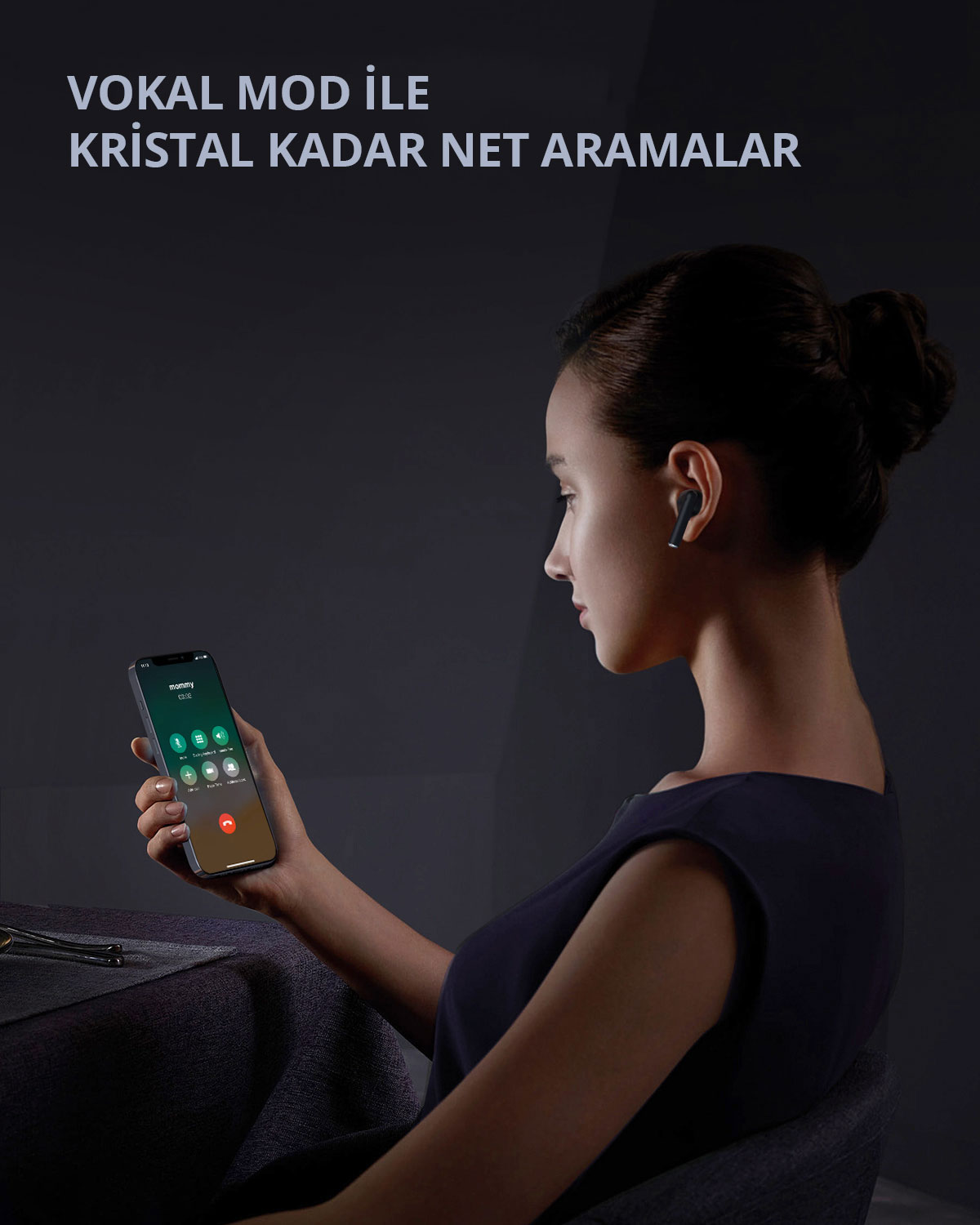 Bir kadın masada oturuyor, siyah kulaklık takmış ve aramdaki bir akıllı telefonu tutuyor.