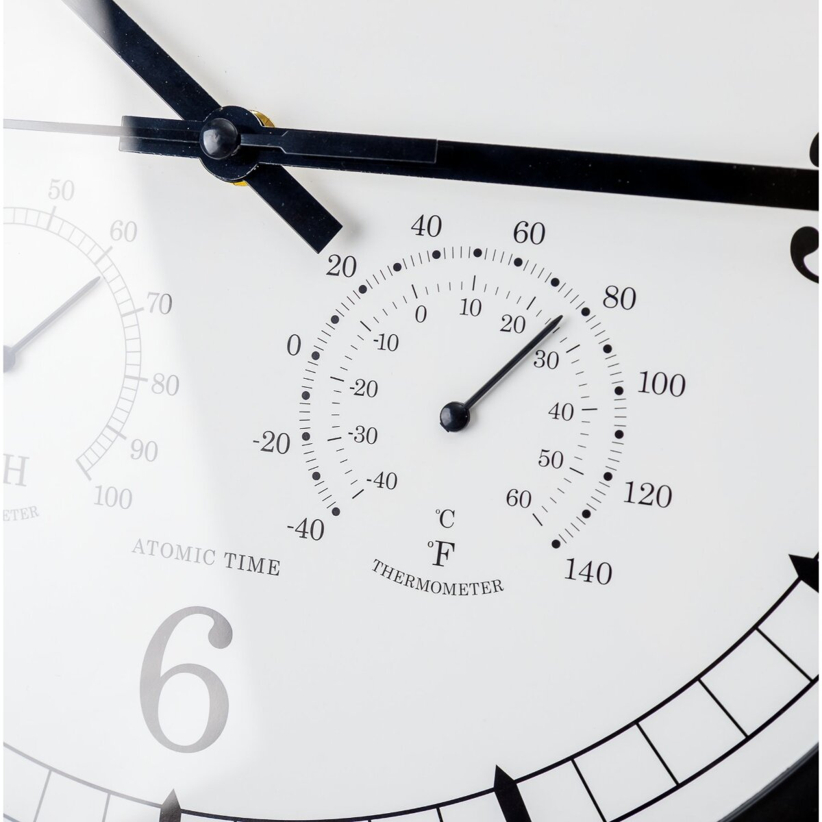 Nahaufnahme eines runden Wanduhrzifferblatts mit Thermometer und Hygrometer.