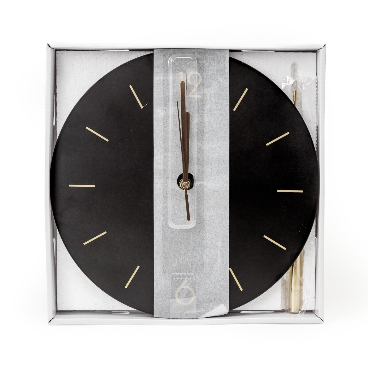 Eine schwarze Wanduhr mit goldenen Zeigern und Indizes in einer weißen Verpackung.