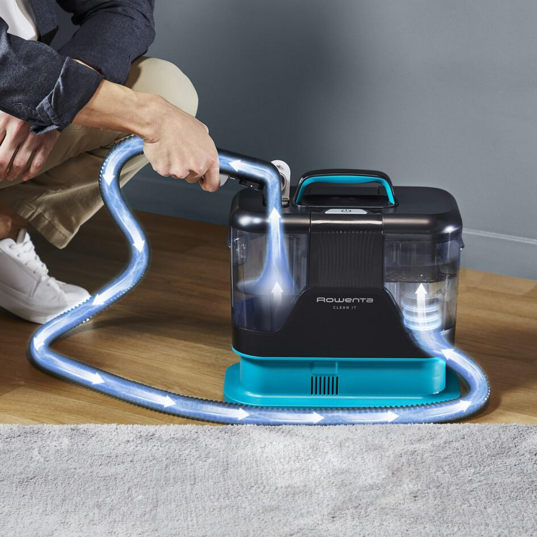Eine Person benutzt einen Rowenta Teppichreiniger mit leuchtenden Pfeilen auf einem Holzboden neben einem Teppich.