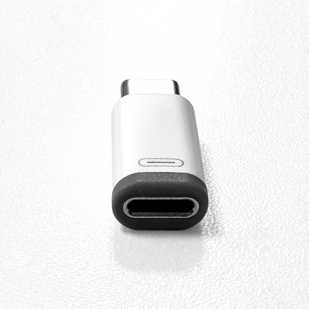 Biało-szary adapter USB-C leżący na białej, fakturowanej powierzchni.
