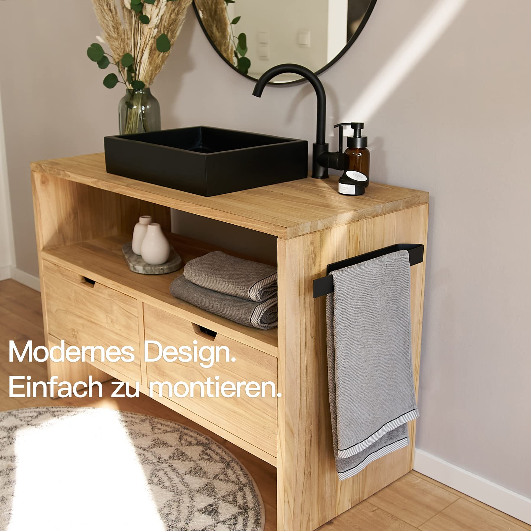 Holz-Waschtisch mit schwarzem Waschbecken, Armatur, Seifenspender, runden Spiegel und Handtuch an der Seite.