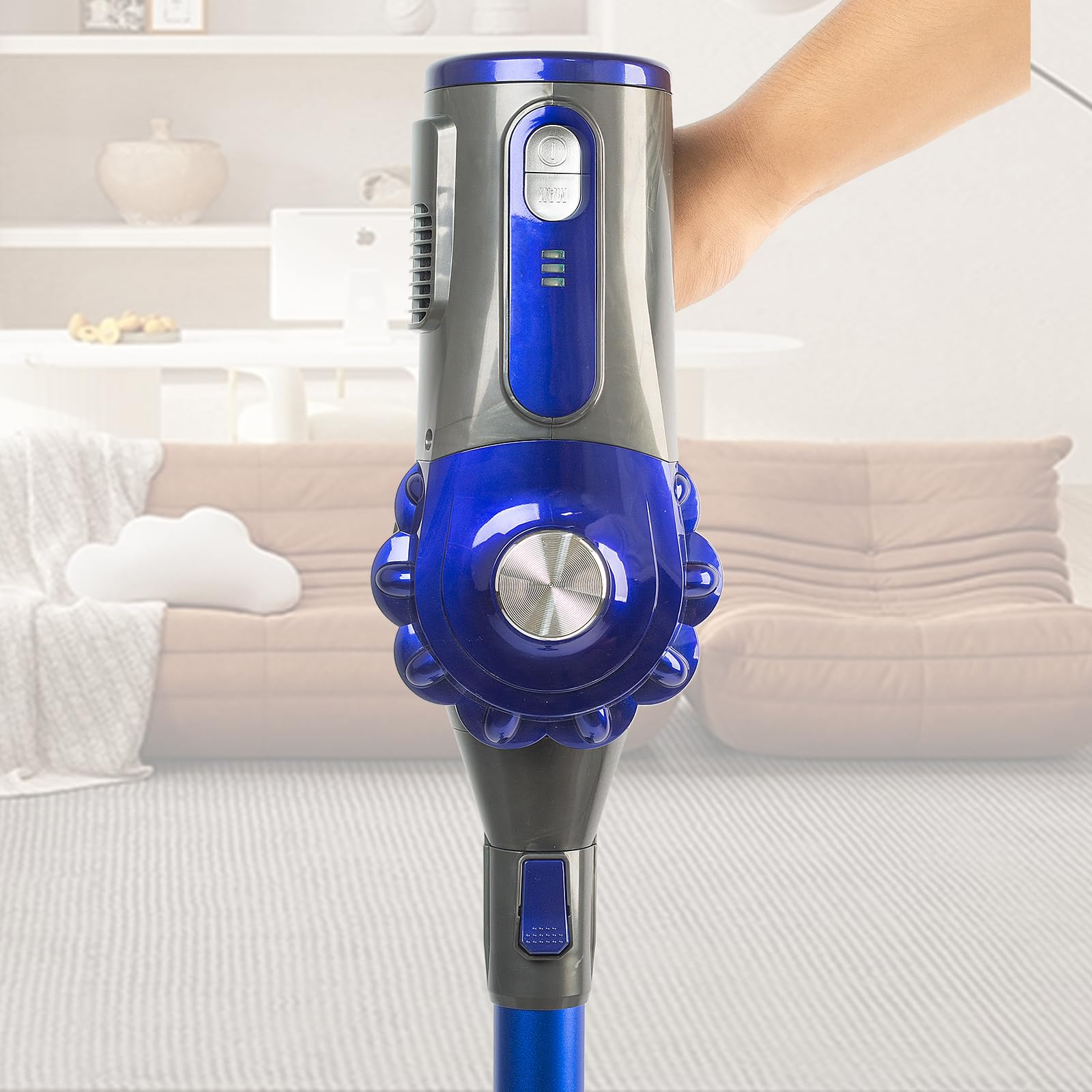 Hand hält blauen und grauen Akkusauger vor unscharfem Wohnzimmer.