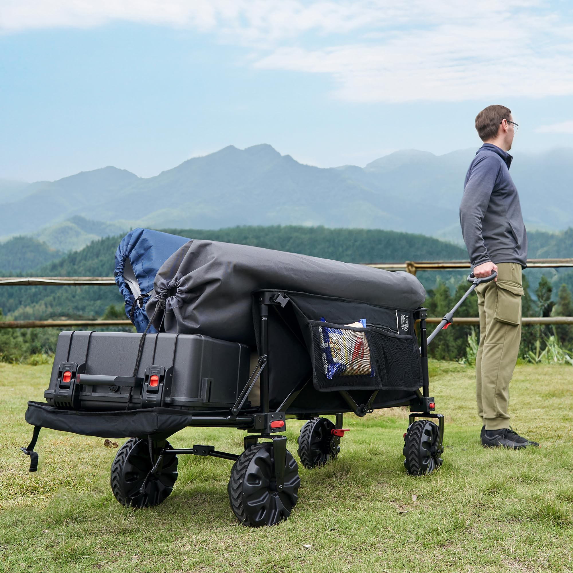 Un homme se tient avec un chariot de transport chargé dans un champ vert avec des montagnes en arrière-plan.
