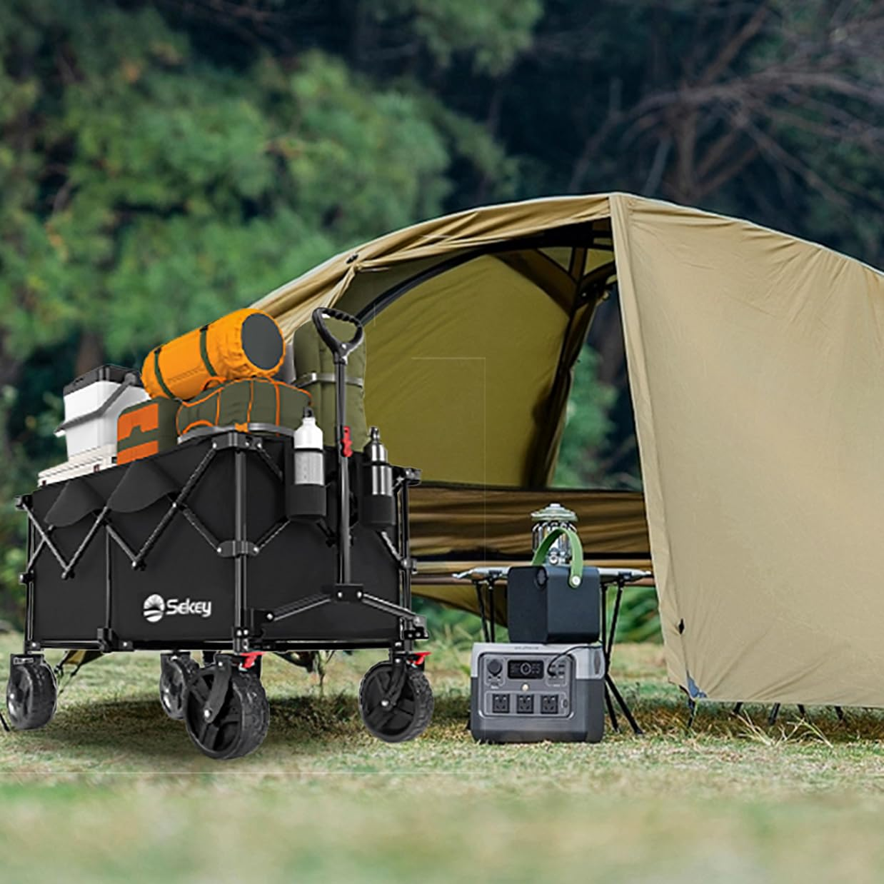 Un chariot de camping noir chargé de matériel est sur l'herbe près d'une tente verte et d'une station électrique.