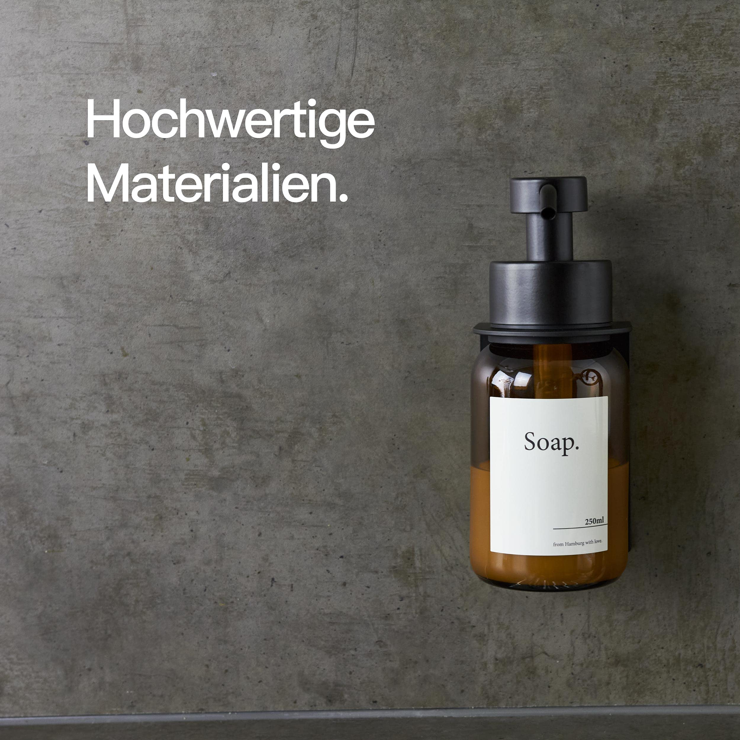 Bernsteinfarbener Seifenspender mit schwarzer Halterung an grauer Wand, Text: Hochwertige Materialien.