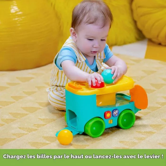 Ein Baby in gestreifter Latzhose spielt auf einer gelben Mustermatte mit einem bunten Spielzeuglastwagen.