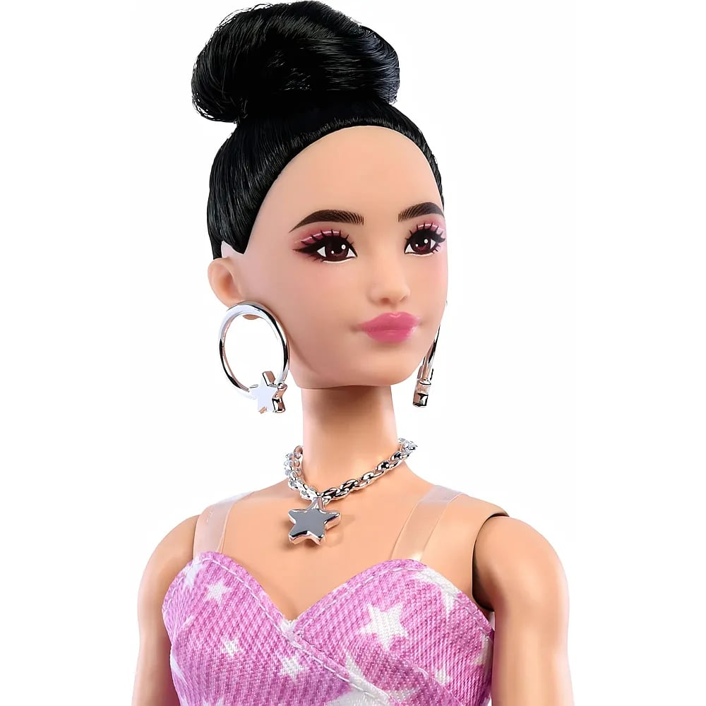 Una muñeca de moda con cabello negro en moño, aretes de argolla y una blusa rosa con estrellas.