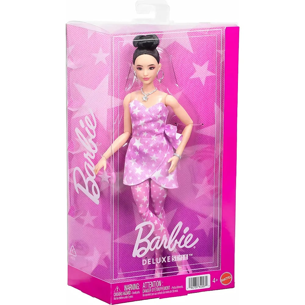 Una muñeca Barbie Deluxe Style con moño negro, vestido rosa con estrellas y pantalones a juego en una caja.