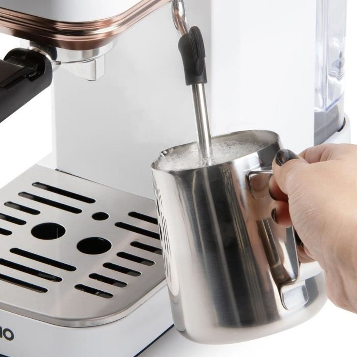 Une main tient un pichet à lait en acier inoxydable sous la buse vapeur d'une machine à espresso blanche.
