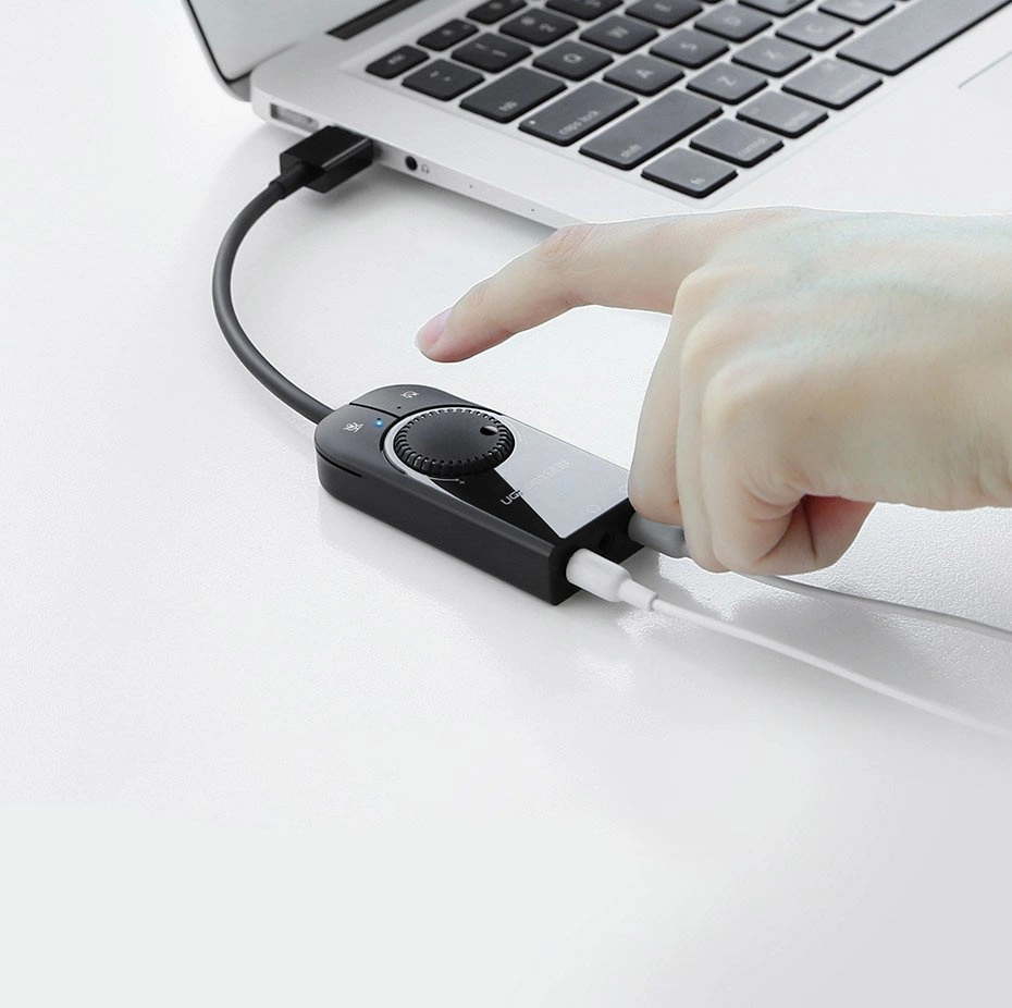 Ręka naciska przycisk na czarnym adapterze audio podłączonym do laptopa.