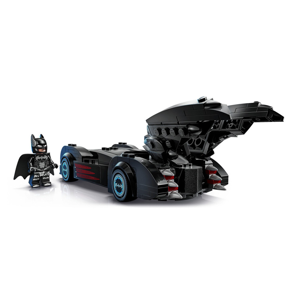 Minifigurka Lego Batman obok dużego czarnego Batmobilu z niebieskimi akcentami kół na białym tle.
