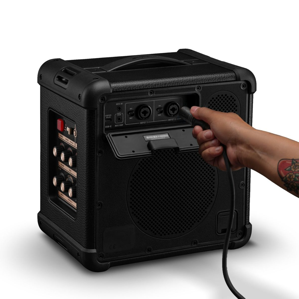 Eine Hand verbindet ein Kabel mit der Rückseite eines schwarzen, tragbaren Gitarrenverstärkers.