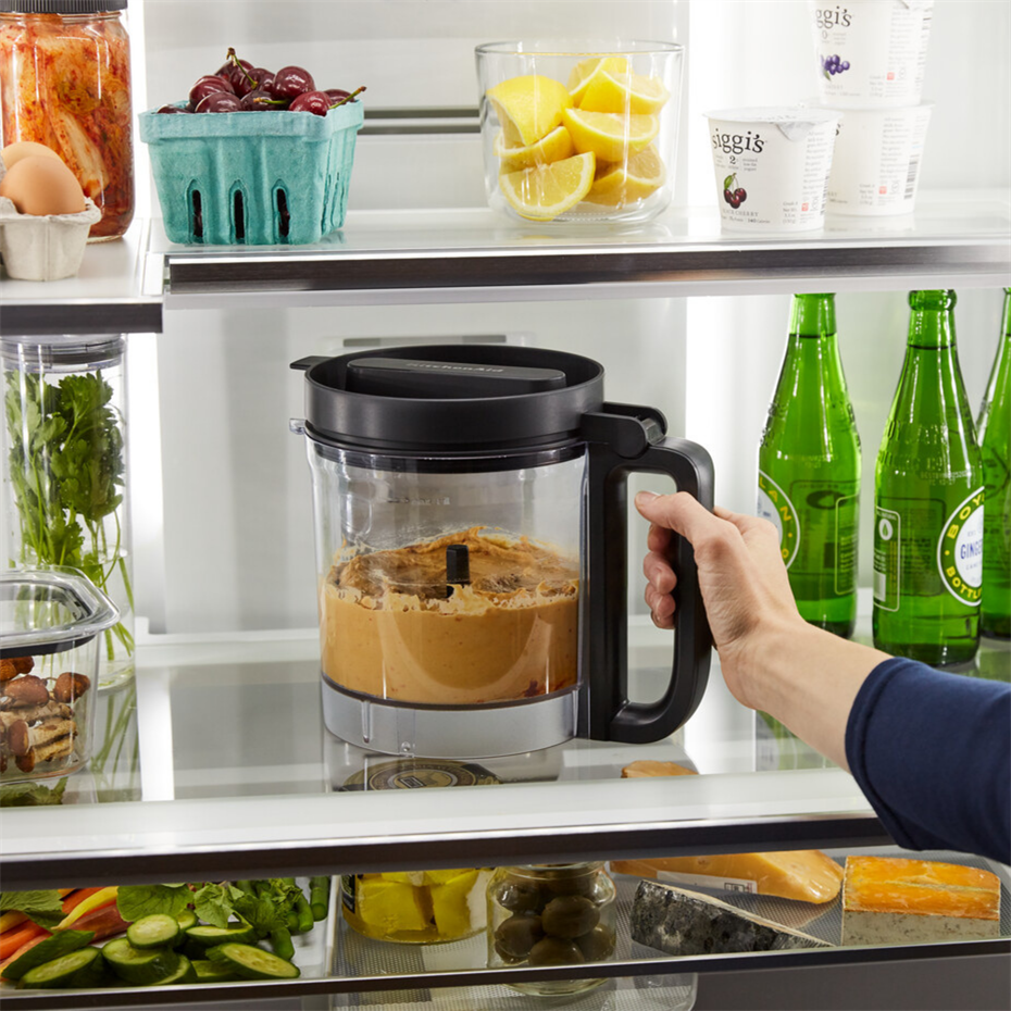 İyi stoklanmış bir buzdolabında fındık ezmesi dolu bir blender tutan bir el.