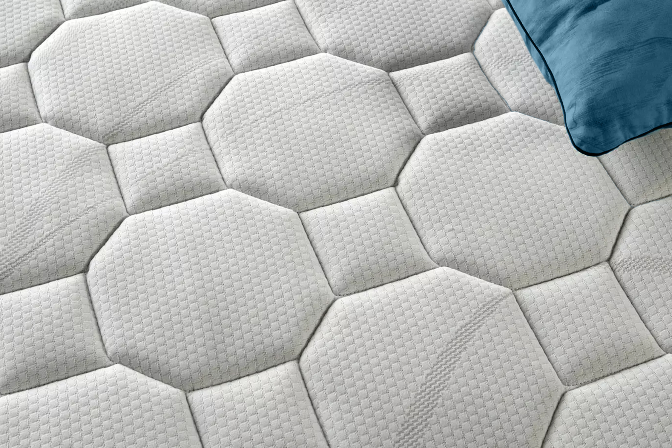 Egy fehér matrac geometriai mintával és egy kék párnával a sarokban.
