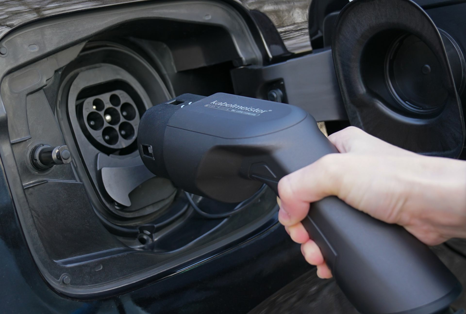 Eine Hand steckt ein schwarzes Ladekabel in die Buchse eines Elektroautos.