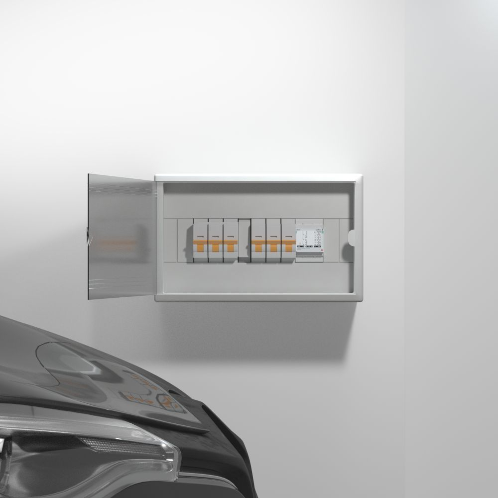 Ein offener Sicherungskasten an einer weißen Wand, teilweise verdeckt durch die Motorhaube eines grauen Autos.