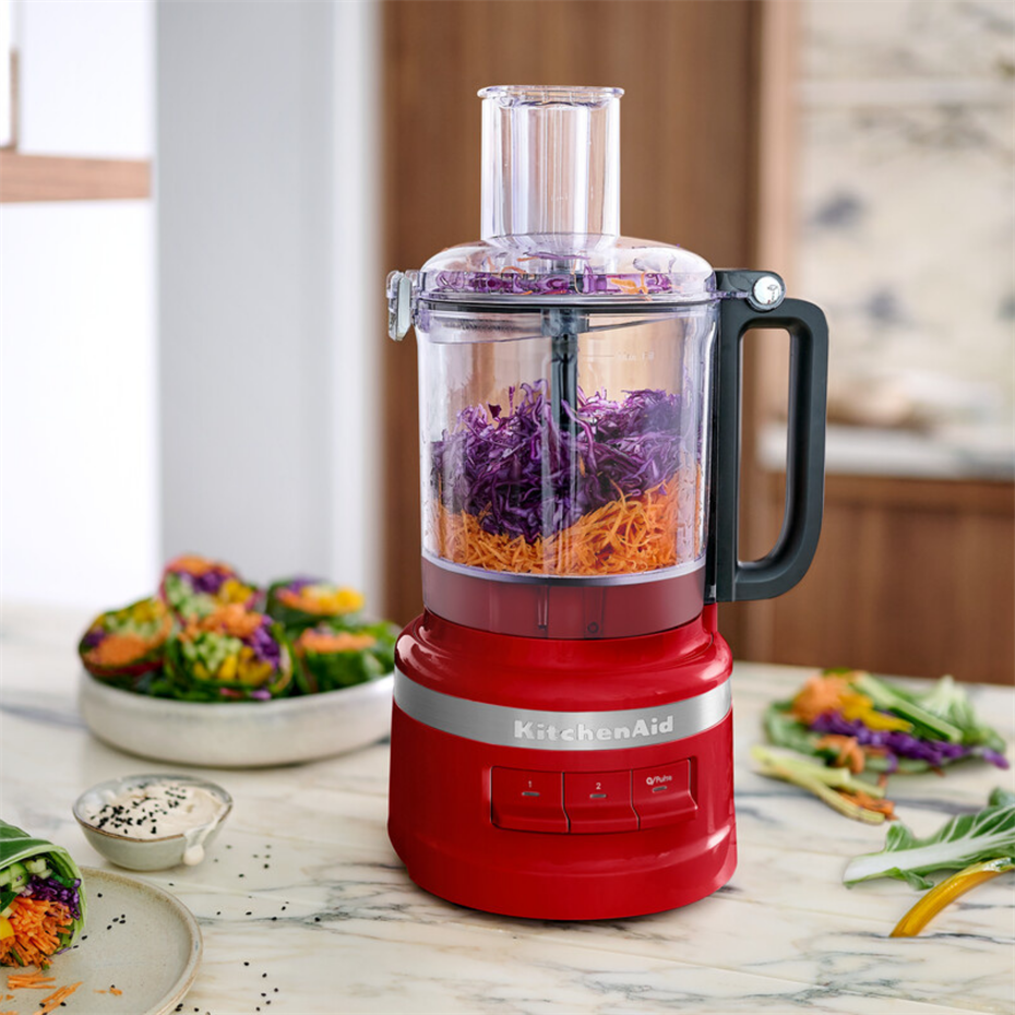 İçinde rendelenmiş kırmızı lahana ve havuç olan kırmızı KitchenAid mutfak robotu.