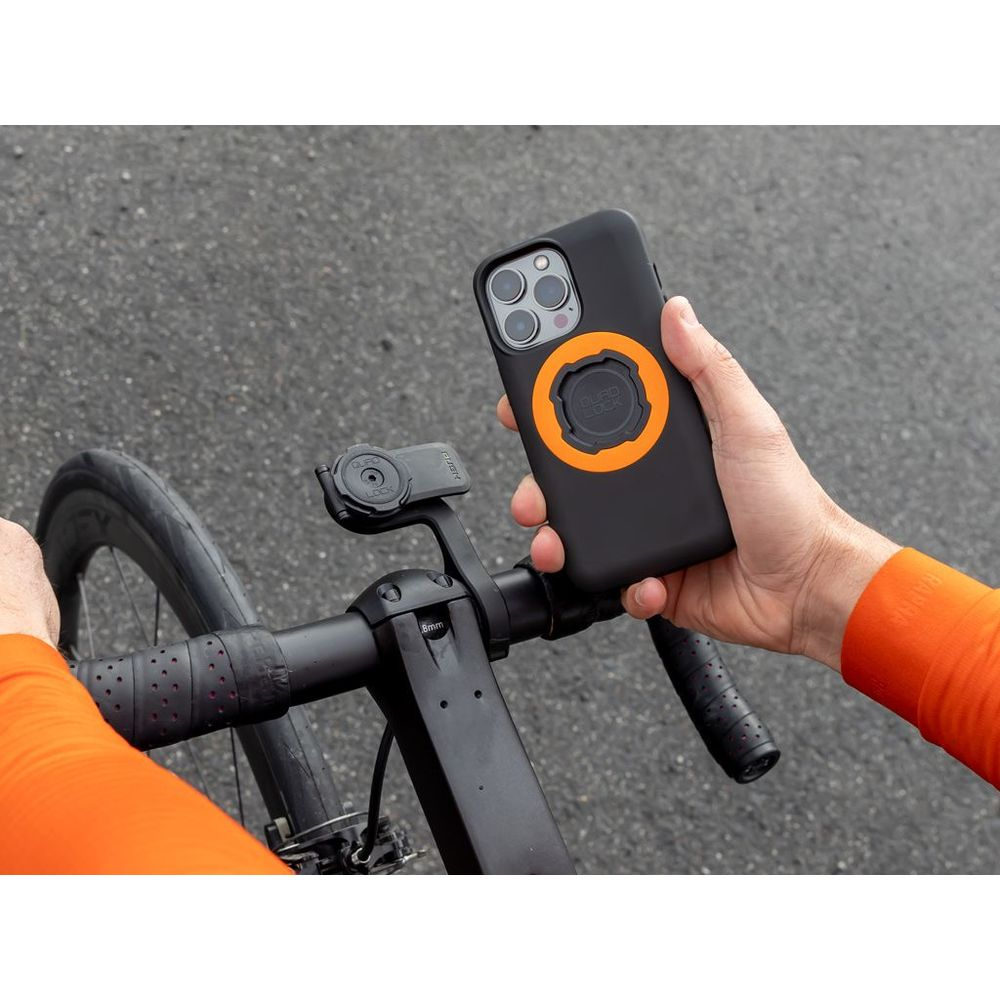 Person hält ein schwarzes Smartphone mit orangefarbenem Ring über einer Fahrradlenkerhalterung.