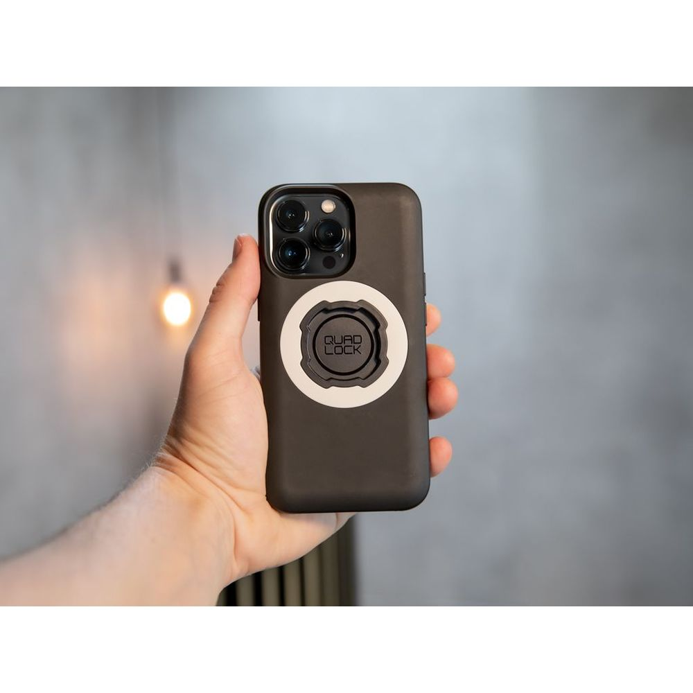 Eine Hand hält ein schwarzes Smartphone mit einer weißen runden Halterung auf der Rückseite vor grauem Hintergrund.