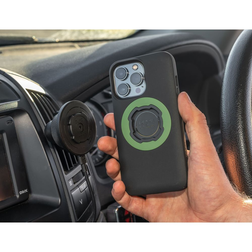 Eine Hand hält ein Handy mit runder grüner Halterung neben einer Autohalterung.