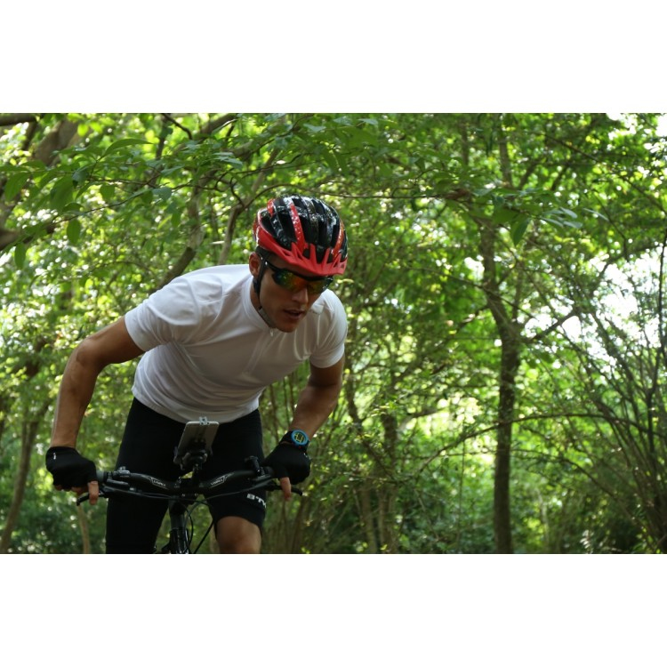 Un ciclista con camisa blanca, casco rojo y gafas de sol monta en bicicleta por un sendero.