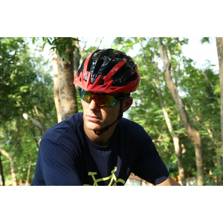 Un ciclista con casco rojo y negro y gafas de sol espejadas en un bosque.