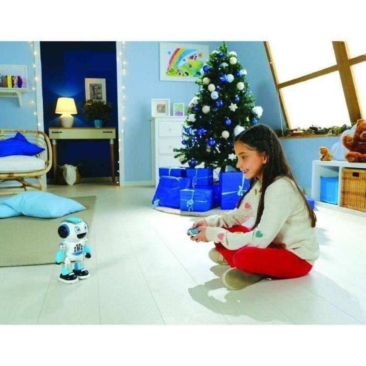 Ein Mädchen sitzt im Wohnzimmer auf dem Boden und steuert einen kleinen weißen und blauen Roboter mit einer Fernbedienung.