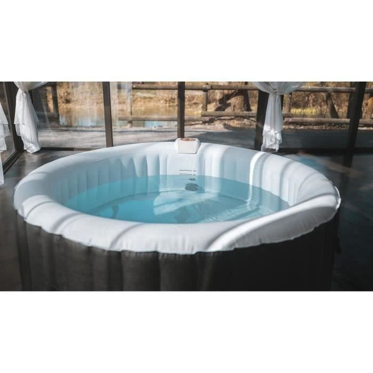Ein runder, aufblasbarer Whirlpool mit klarem Wasser steht in einem Raum mit großen Glasfenstern und Blick ins Freie.