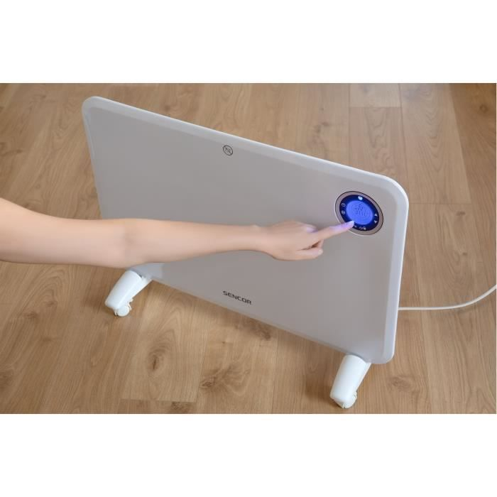 Eine Hand bedient das digitale Display eines weißen Sencor Konvektionsheizers auf einem Holzfußboden.