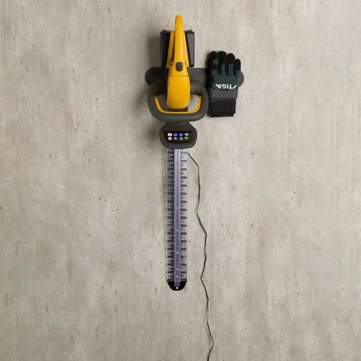 Eine gelb-graue Heckenschere hängt senkrecht an einer strukturierten Betonwand, daneben ein Handschuh.