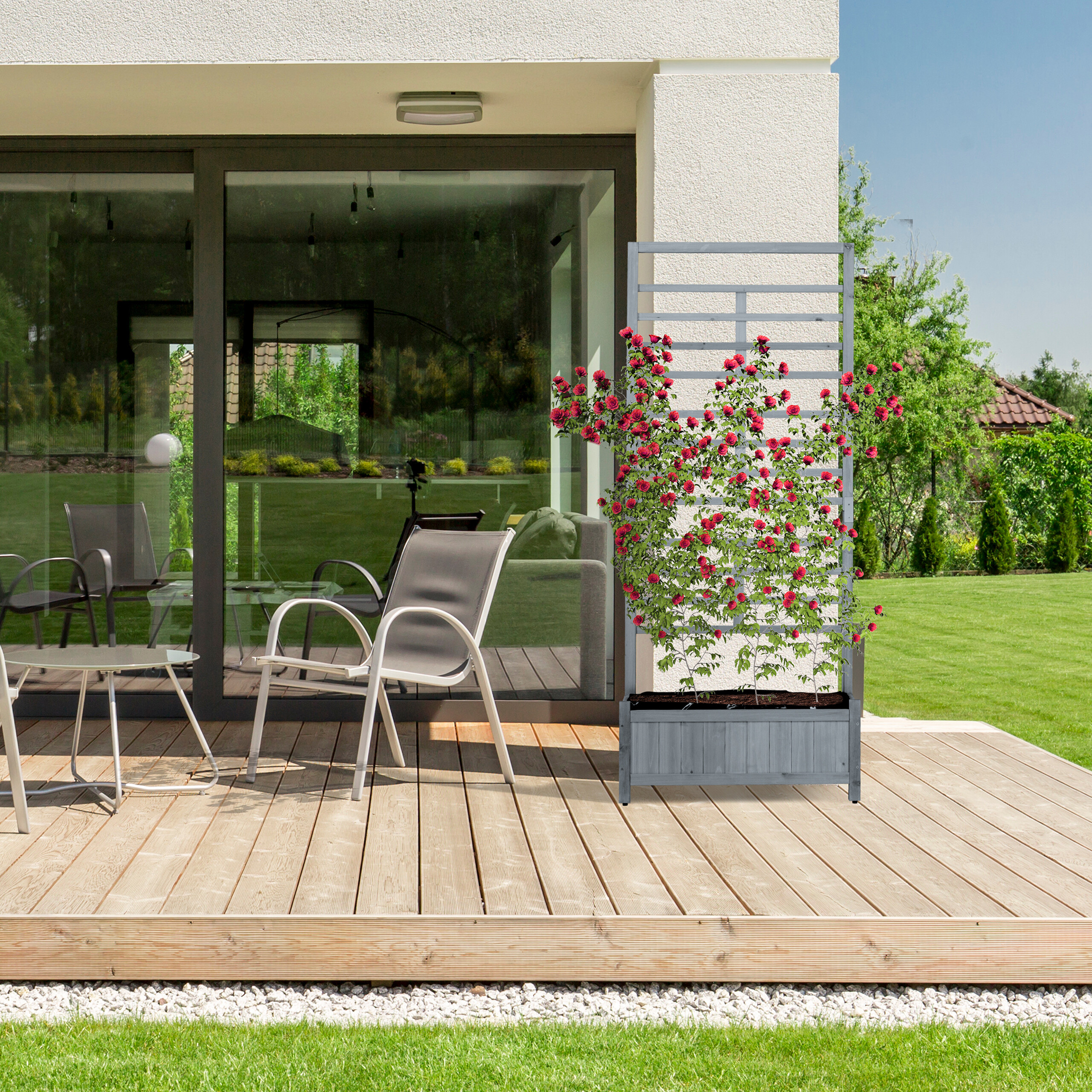Ein Holzblumenkasten mit Rankgitter und roten Rosen steht auf einer Terrasse mit Stühlen und Rasen.
