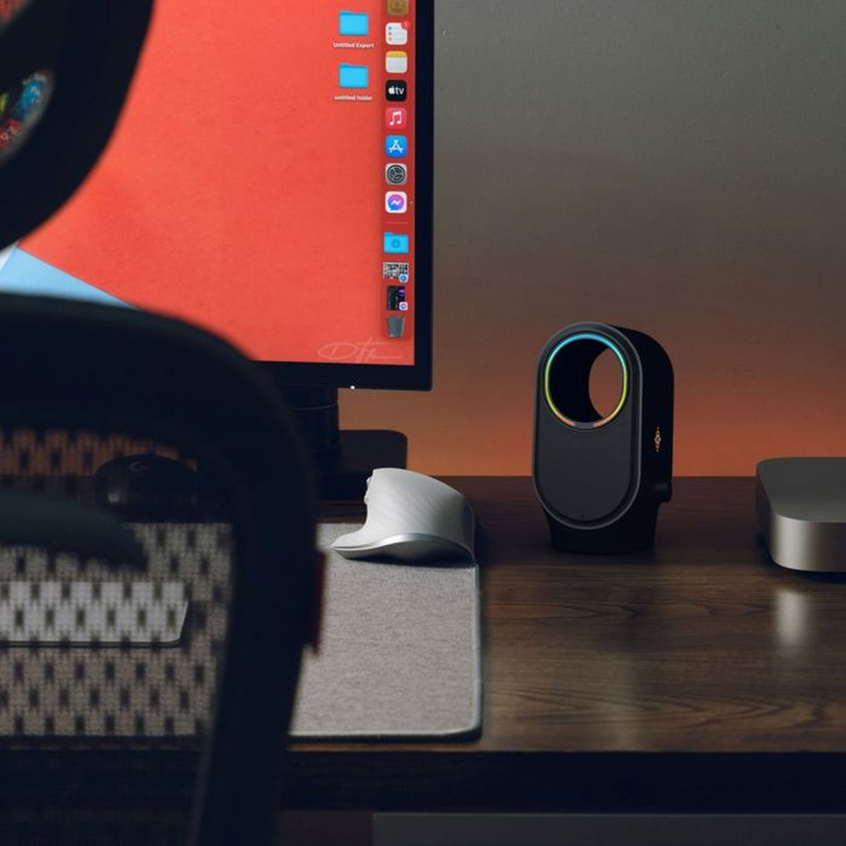 Ein Schreibtisch mit Monitor, einem runden Ventilator mit Lichtern, ergonomischer Maus und Stuhl.